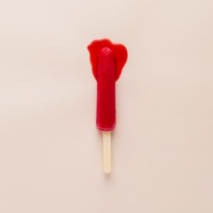 Lolly pop stick with red ice and red leaking onto pale pink background